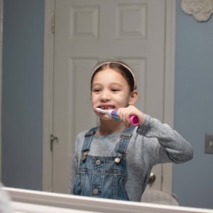 A mirrored reflection of a young girl brushing her teeth.